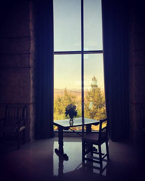 A quiet interior scene featuring a small table and chairs by a large window overlooking trees in soft natural light. Suitable for concepts related to relaxation, hospitality spaces, peaceful mornings, cafes, and lifestyle inspiration.