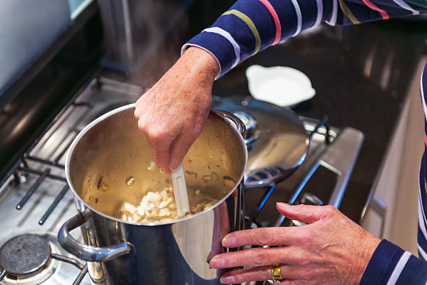 Close-up image of a woman's hands using a spoon to stir ingredients in a pan on a gas hob on the kitchen counter.