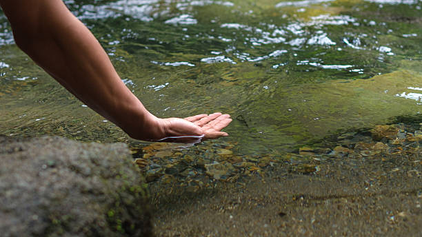 istock Calm Hand Gently Touching Clear River Water Over Pebbles and Rocks Along Quiet Shore Edge 2245848422