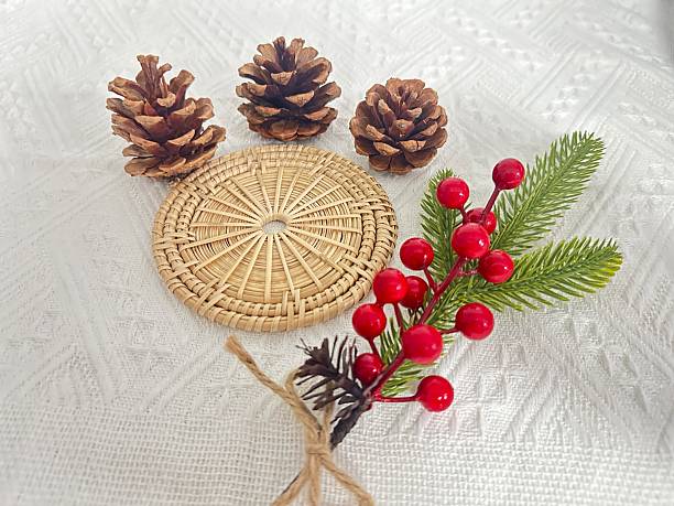 istock Natural decor elements featuring pine cones, woven coaster, red berries, and greenery on an elegant white tablecloth for festive ambiance and creativity 2245851118