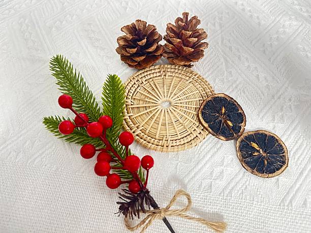 istock Festive arrangement with pinecones, dried oranges, decorative berries, and woven mat on a textured white background for holiday inspiration and decoration 2245851149