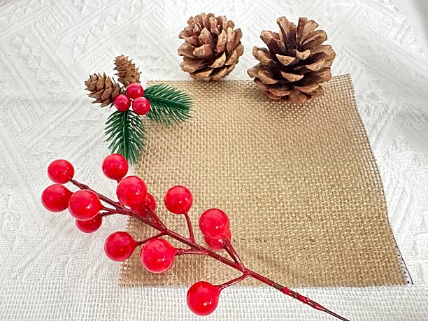 istock Rustic holiday decor arrangement featuring pinecones, red berries, and burlap fabric on a textured white background for festive celebrations 2245851266