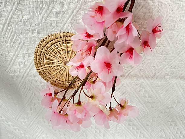 Delicate Pink Cherry Blossom Branch on Woven Mat with Textured White Background, Perfect for Spring and Floral-Themed Projects