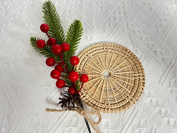 istock Rustic holiday decoration featuring natural elements, red berries, pine branches, and woven plate resting on textured white fabric background 2245851436
