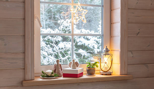istock Christmas window decor with Advent candle, knitted angels, glowing lantern, gift box and Christmas cactus, cozy wooden Scandinavian interior with snow outside, warm holiday atmosphere, festive light 2245853049
