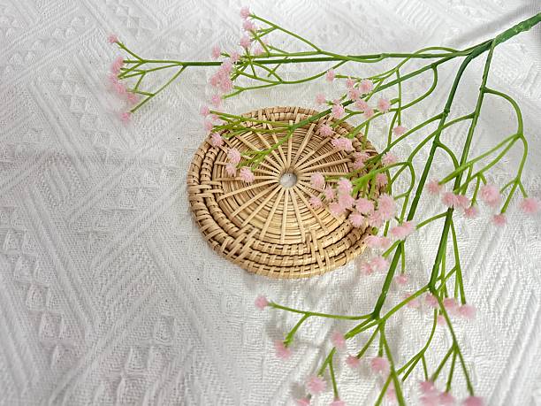 istock Delicate pink flowers arranged gracefully on a woven wicker coaster against a textured white fabric background, creating a serene and inviting atmosphere. 2245853078