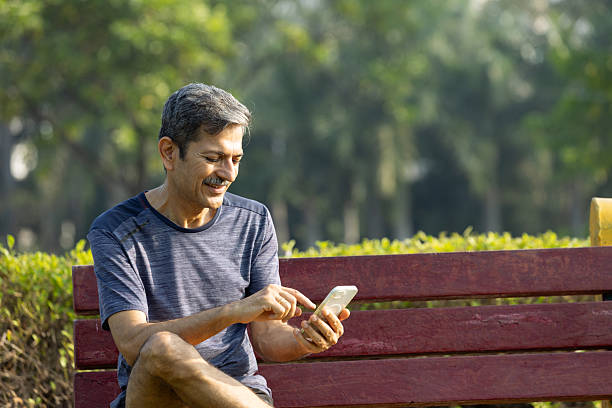 istock Indian Senior Man Sitting on Park Bench Using Smartphone to Relax After Exercise 2245853142