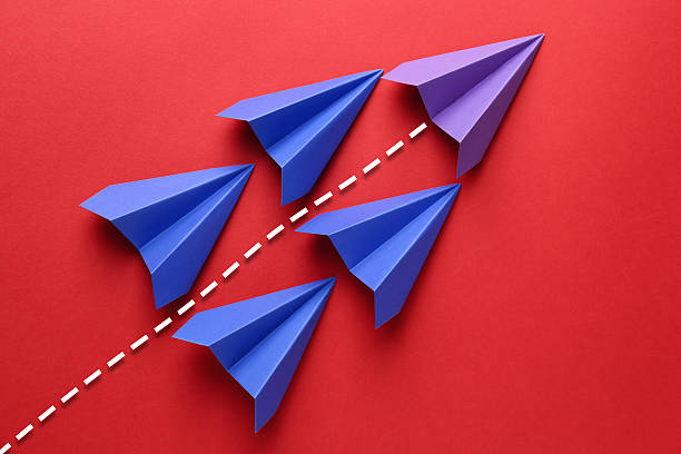 istock Purple paper plane with flight path among blue ones on red background. Dashed line for trajectory 2245854448