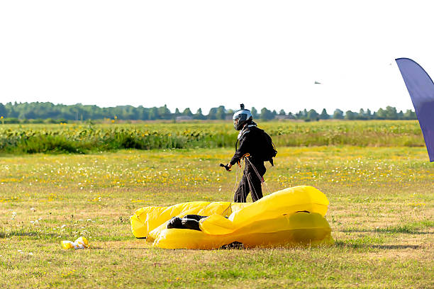 Skydiver packs yellow parachute on open field after landing, preparing for next jump