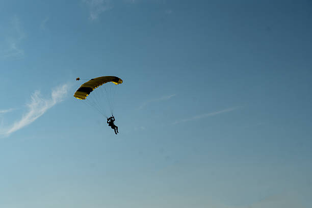 istock Skydiver with yellow canopy descending toward landing zone in clear blue sky 2245866945