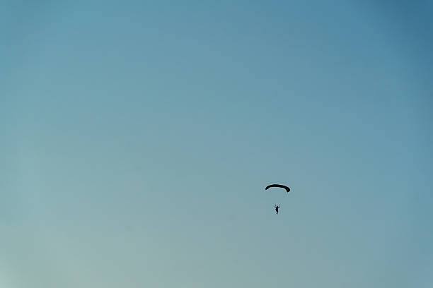 A lone skydiver flies with an open canopy high above an open landscape, captured from the ground. The moment emphasizes adrenaline, freedom, and skill as the parachute glides toward a safe, controlled landing. Perfect for adventure, sport, and outdoor lifestyle themes.