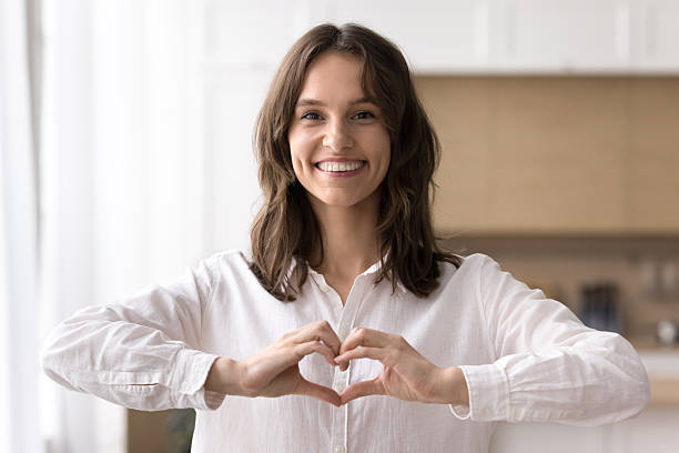 istock Grateful millennial woman looking at camera making tender finger heart 2245867400