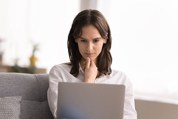 istock Busy young female sitting on couch focused on notebook screen 2245867579
