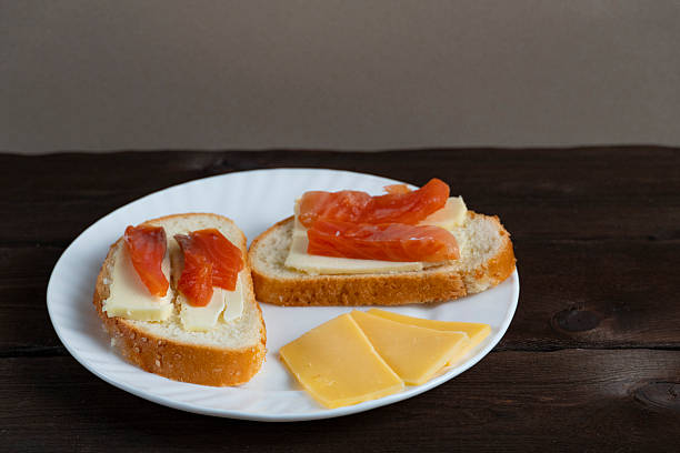 Homemade sandwiches with butter and red fish slices on white plate with cheese on dark wooden background. Perfect for breakfast or food blog themes