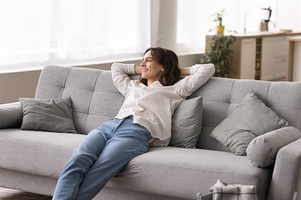 istock Smiling young female lean back on sofa hands behind head 2245868995