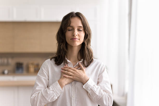 istock Young woman with closed eyes holding folded hands on heart 2245871006