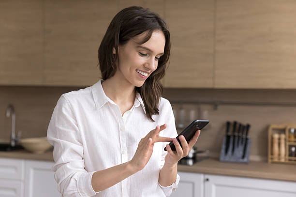 istock Smiling young girl typing message on phone at home kitchen 2245875521