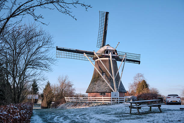 Winter landscape in Holland (the Netherlands) in a rural area with a windmill in a meadow, a fence, a canal, snow and fog at sunrise.