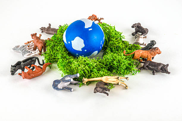 A blue globe on green moss, surrounded by various toy animals lying on ground. the disappearance of wild animals as a result of irresponsible human activity