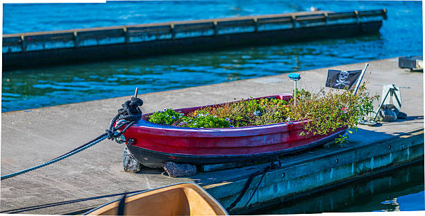 An overturned fishing boat placed on a grassy field near the ocean, surrounded by wildflowers under a cloudy sky. The scene evokes calmness and the essence of coastal life.