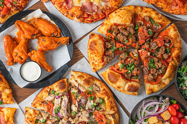 Assorted pizzas and buffalo wings with salads and dipping sauces arranged on parchment paper.