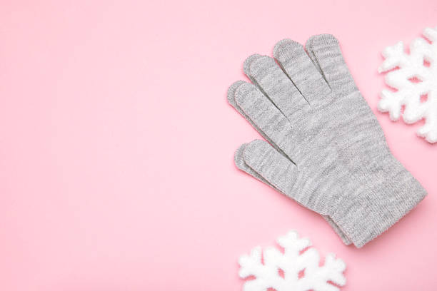 Warm woolen knitted gloves with white snowflakes on pink background. Space for text