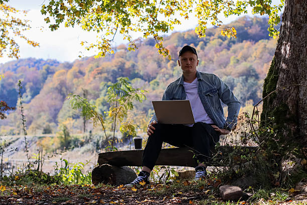 istock Man leans forward engaged with laptop amid colorful fall leaves and trees 2245887334