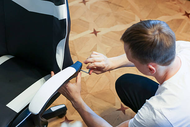 istock Man assembling black and white gaming chair with screwdriver on wooden floor. 2245888542