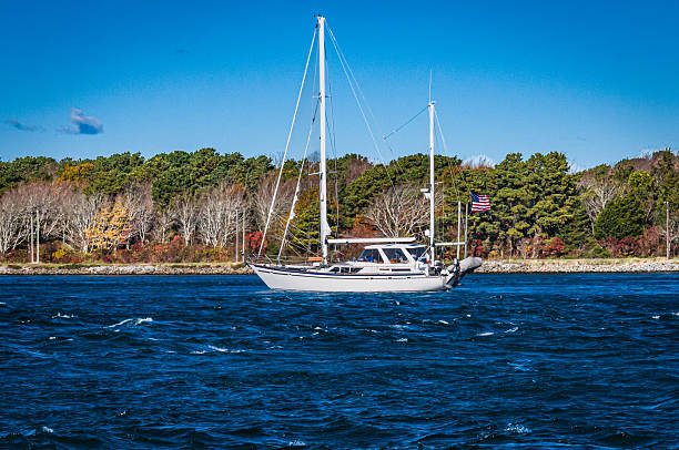 A white sailing yacht heads west on the Cape Cod canal while a strong Novermber wind kicks up white cap waves on the water surface