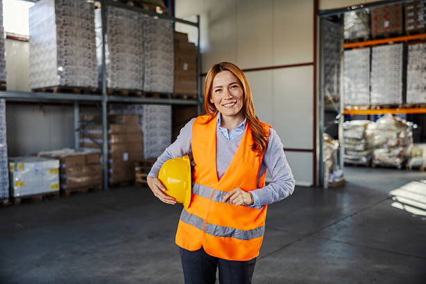 istock Female warehouse worker holding hard hat smiling 2245892363