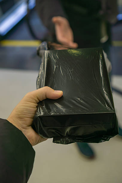 istock Close-up of two people exchanging a black plastic-wrapped package, symbolizing delivery, confidential transaction, or secretive exchange concept. 2245897396