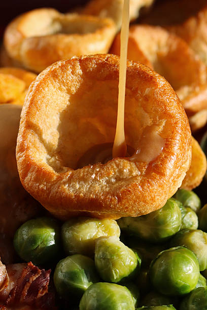 Full frame image Sunday roast dinner with all the trimmings, gravy being poured on Yorkshire pudding, roast chicken with crispy, golden skin, surrounded by side dishes of Brussel sprouts, roast potatoes, focus on foreground