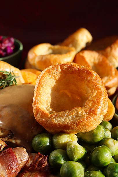 Image of Sunday roast dinner with all the trimmings, Yorkshire pudding , roast chicken with crispy, golden skin, surrounded by side dishes of Brussel sprouts, roast potatoes, pigs in blankets, bowl of braised red cabbage, focus on foreground