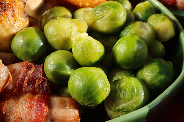Stock photo showing close-up, elevated view of  a traditional roast chicken dinner served for Sunday lunch on an oval, green serving plate, featuring juicy roasted chicken, golden potatoes, pigs in blankets (pork cocktail sausages wrapped in bacon) and tender Brussels sprouts. This stock image highlights hearty home-cooked meals, comfort food, and family dining.