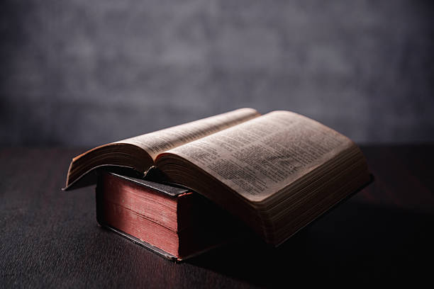 istock Open Bible on black background. Religion concept. a Christian sat reading an open Bible the holy book of Christianity deepening their faith in God and Jesus Christ, the foundation of their religion. 2245926424