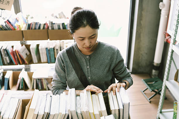 An Asian woman is in a second-hand bookstore, choosing second-hand books. It's a second-hand store