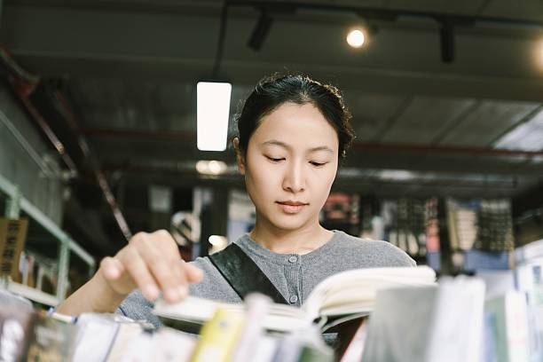 An Asian woman is in a second-hand bookstore, choosing second-hand books. It's a second-hand store