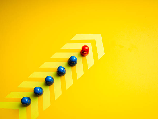 istock Leadership concept with red figure leading blue team figures forward on arrow path on yellow background. Symbolizes team direction, business leadership, innovation, and strong vision for success. 2245926925