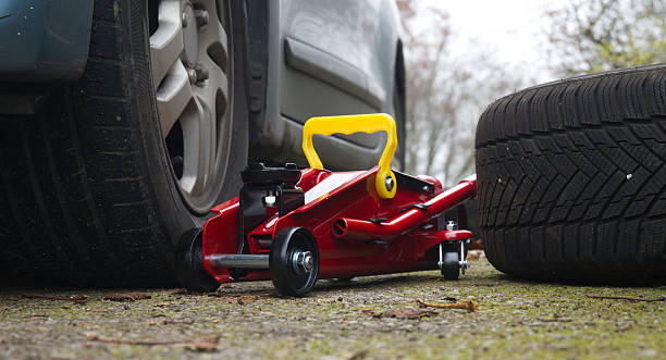 istock Red Hydraulic Floor Jack Under Car With Yellow Handle Beside Spare Tire On Ground 2245927672