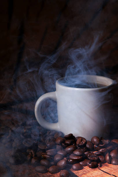 A close-up of the top of a steaming hot cup coffee with steam rising as the light from the sun rises through the window of a diner.