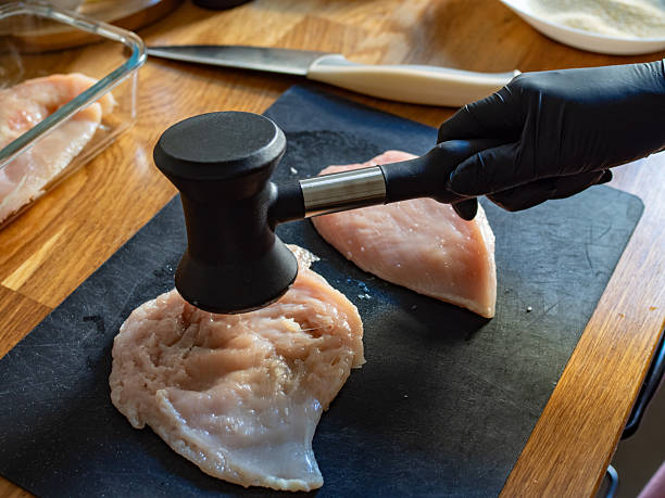 Cooking breaded chicken cutlets- pounding chicken breast, close-up