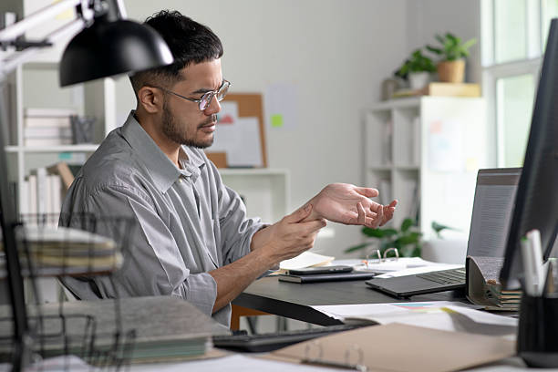 istock Businessman suffering from wrist pain while working on computer, Businessman massaging his hand and wrist after long hours in front of a computer 2245939398