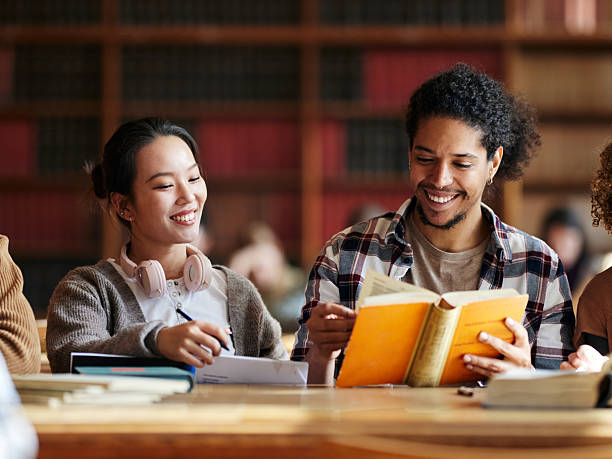 istock Happy university friends studying from book in library. 2245942273