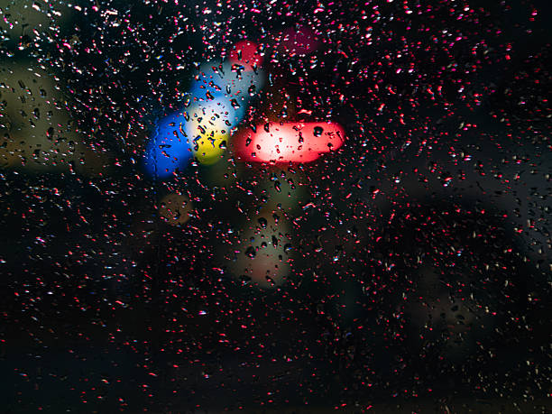 Raindrops on windowpane overlooking vibrant city lights during evening rainstorm