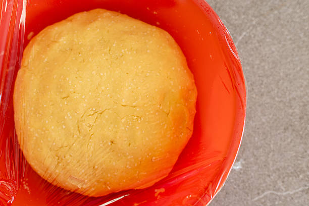 Raw dough being kneaded in a red mixing bowl on a gray kitchen surface. Close-up, home cooking preparation for making cheese sticks.