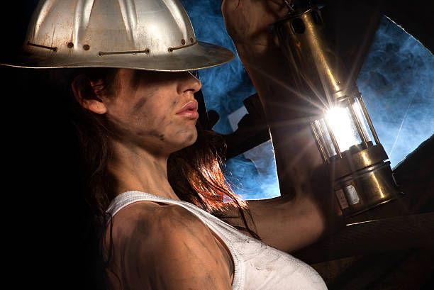 Portrait of a miner holding a metal ring, covered in dust, in a dark tunnel, next to an electrical panel