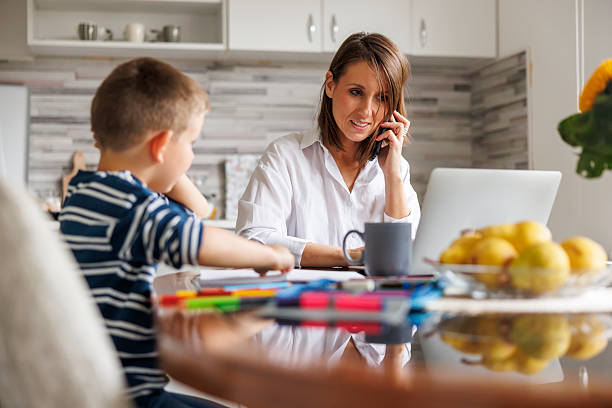istock Mother having phone conversation and working while son doing homework at home 2245959461