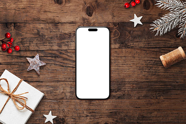 istock Smartphone with blank white screen on rustic wooden background, surrounded by Christmas decorations, pine branches, and festive ornaments 2245959529
