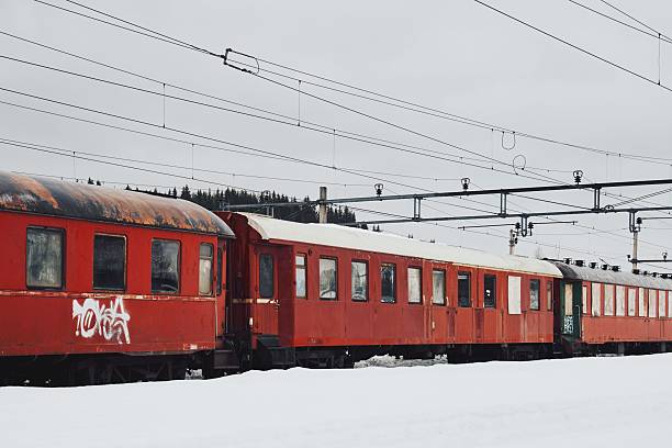 Eina, Norway – March 09, 2023: A train is pictured parked on a set of railroad tracks in a wintery setting, surrounded by snow-covered trees and electrical power lines