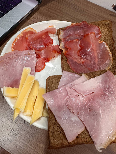A casual meal featuring thinly sliced pink ham, rich cured pork, and yellow cheese wedges, served alongside dark wholemeal bread on a warm wooden table. Perfect for a quick lunch or snack.